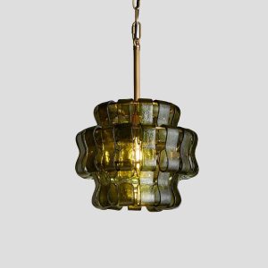 Wavy green glass pendant light with antique brass hardware turned on creating warm ambient glow
