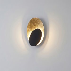 Modern gold leaf eclipse LED wall sconce featuring a matte black front disc and warm indirect backlighting.